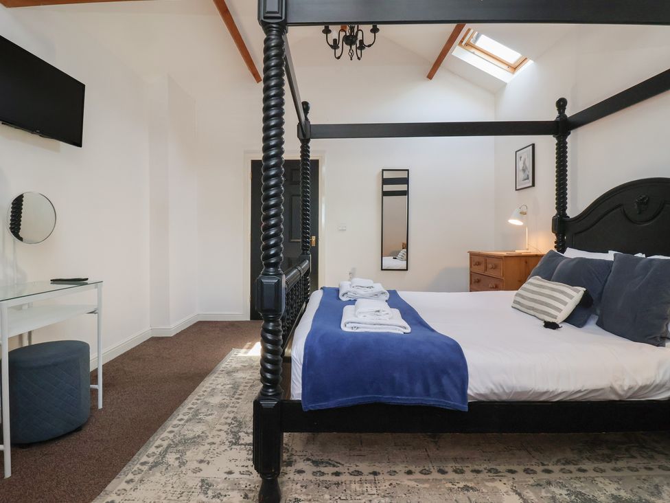 A bedroom with a four poster bed a rug a chest of drawers and a wall mounted television at Guillemot in Flamborough