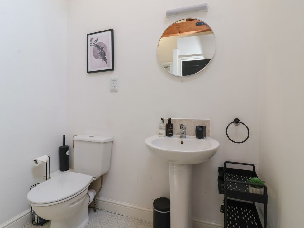 A bathroom with a toilet sink round mirror and a storage rack at Guillemot in Flamborough