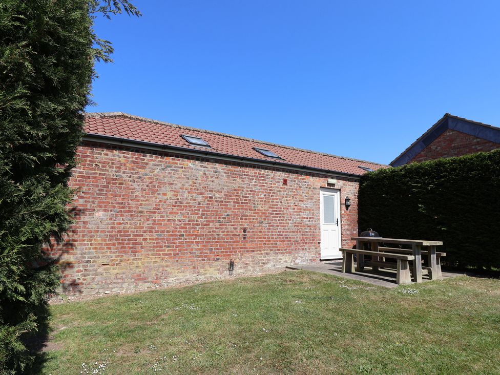 A brick building with a red tiled roof and white door next to a wooden picnic table on grass at Guillemot in Flamborough