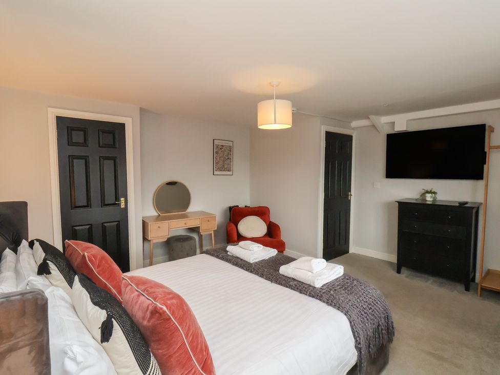 A bedroom with a bed, towels, mirror, chair, tv, and dresser at The Pheasantry in Flamborough