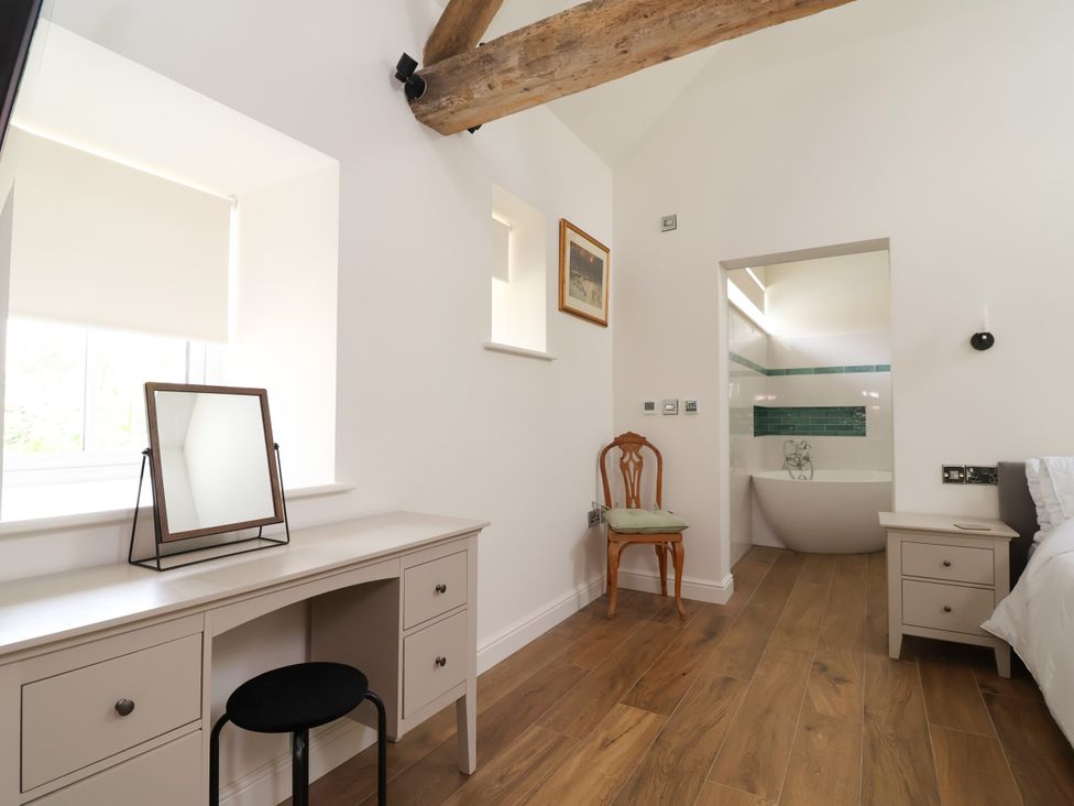 A bedroom with a desk and chair near a bathroom entrance at The Barn in Tafarn-Y-Gelyn
