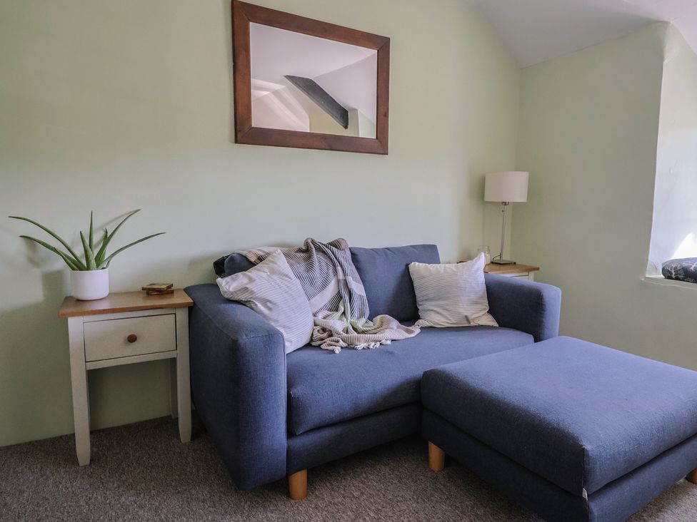 A sitting room with a blue sofa and ottoman two side tables with a plant and lamp and a wall mirror at Eggardon Rest in Askerswell near Bridport