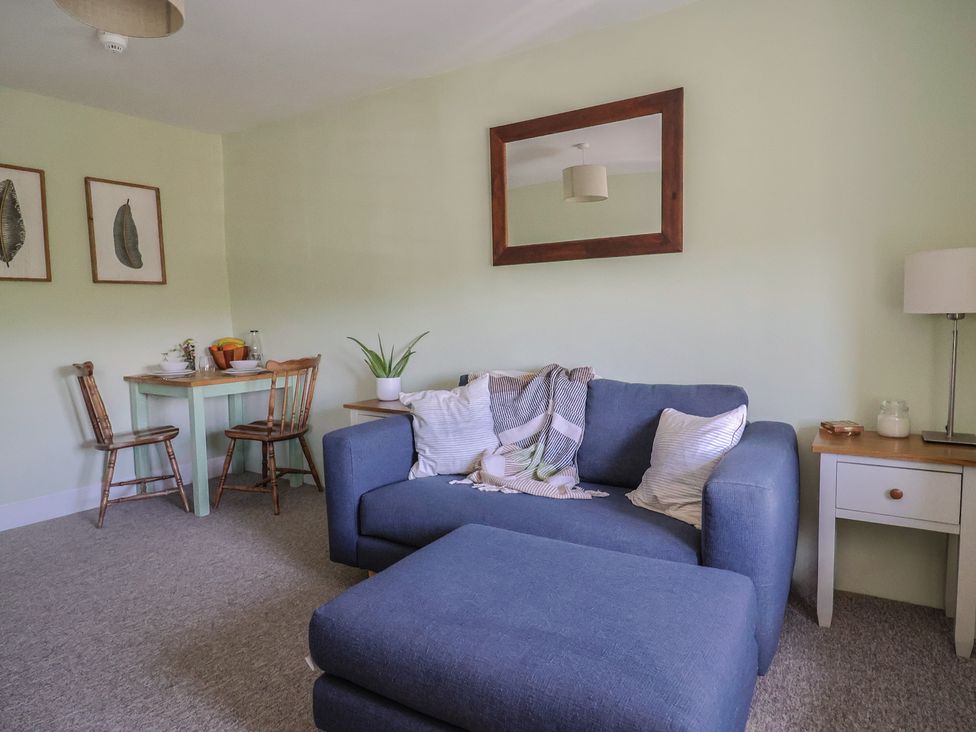 A living room with a blue sofa and ottoman a small dining table with two wooden chairs and a large mirror on the wall at Eggardon Rest in Askerswell near Bridport