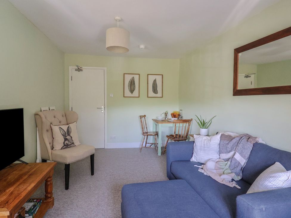 A living room with a blue sofa, wooden table, armchair with a rabbit cushion, small dining table with two chairs, and framed leaf prints at Eggardon Rest in Askerswell near Bridport