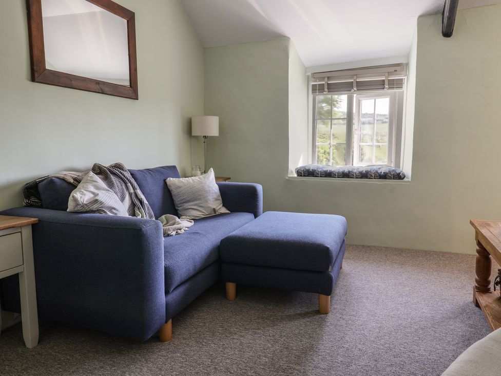 A living room with a blue sofa and ottoman next to a window with a cushion at Eggardon Rest in Askerswell near Bridport