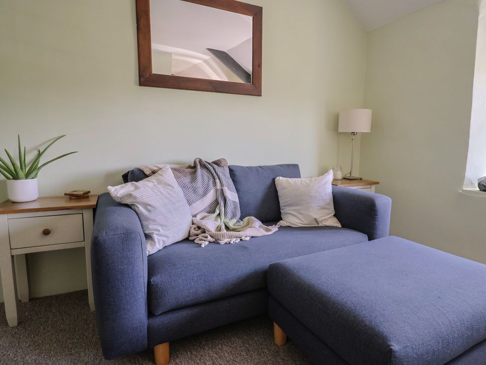A living room with a blue sofa and ottoman a wooden side table with a plant and another side table with a lamp below a mirror on the wall at Eggardon Rest in Askerswell near Bridport