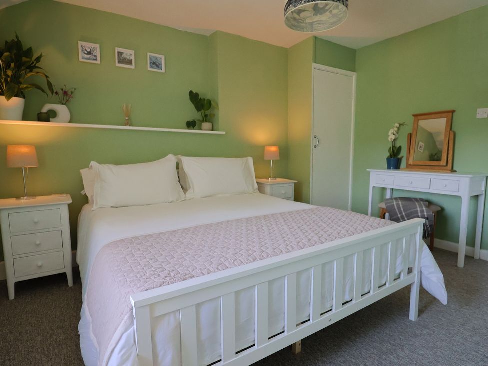 A bedroom with a white bed and bedside tables with lamps and a dressing table at Eggardon Rest in Askerswell near Bridport