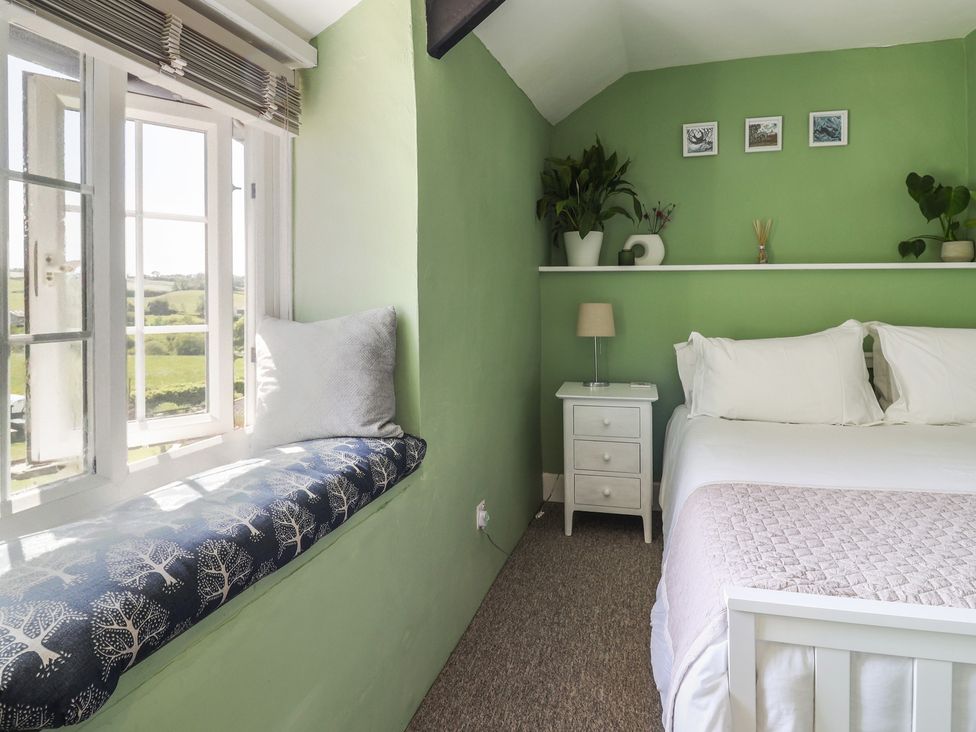 A bedroom with a white bed, green walls, a nightstand with a lamp, and a window seat with a cushion at Eggardon Rest in Askerswell near Bridport