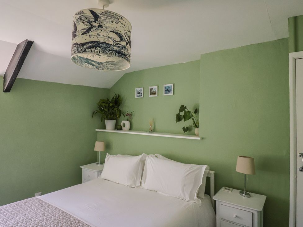 A bedroom with a white bed and pillows two bedside tables with lamps plants on a shelf above the bed and a ceiling light with bird designs at Eggardon Rest in Askerswell near Bridport