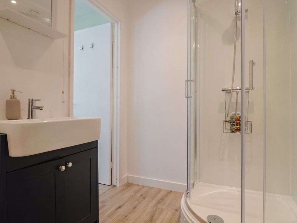 A bathroom with a sink and cabinet next to a curved glass shower enclosure at Eggardon Rest in Askerswell near Bridport