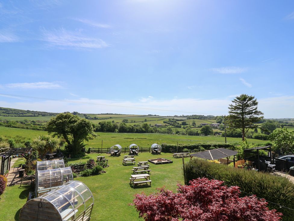 An outdoor garden area with picnic tables wooden pod shelters and green fields in the background at Eggardon Rest in Askerswell near Bridport