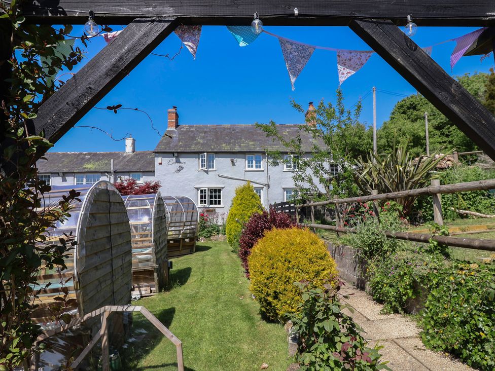 A garden with bushes and plastic-covered seating pods in front of a white cottage at Eggardon Rest in Askerswell near Bridport