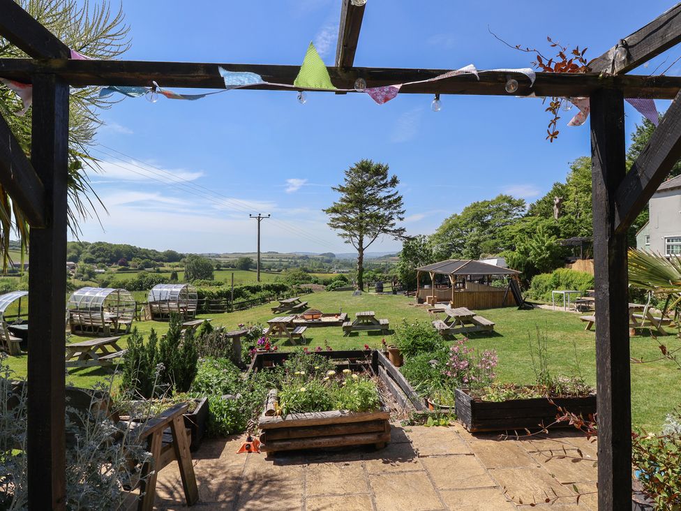 A garden with picnic tables small greenhouses and a wooden gazebo at Eggardon Rest in Askerswell near Bridport