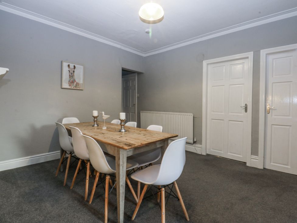 A dining room with a wooden table and white chairs at Penrhyn Arms Apartment in Llandudno