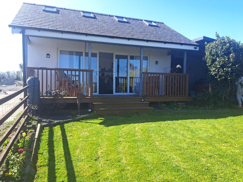 A house with a wooden deck and steps leading to a lawn at Capel Park (Tyddynod Bach) in Llandyfrydog near Llanerchymedd
