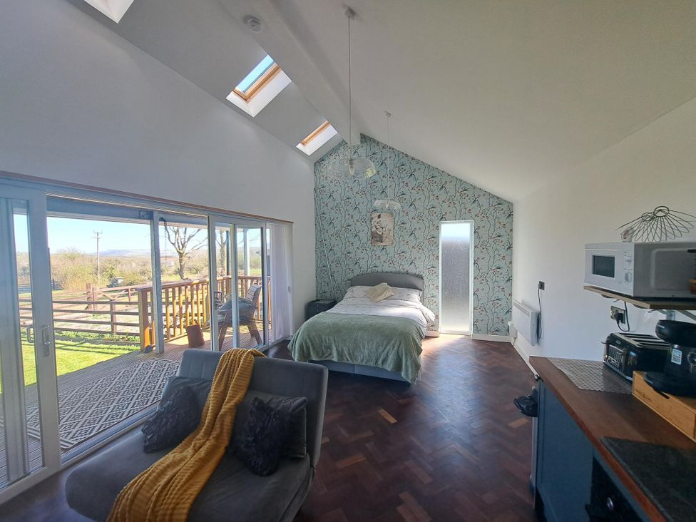 A room with a bed, sofa, kitchen counter with appliances, and sliding glass doors opening to a balcony at Capel Park Tyddynod Bach in Llandyfrydog near Llanerchymedd
