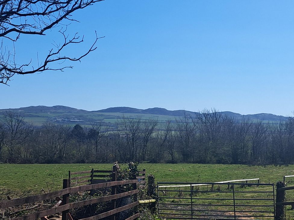 A grassy field with a metal gate and wooden fence with hills and trees in the background at Capel Park Tyddynod Bach in Llandyfrydog near Llanerchymedd