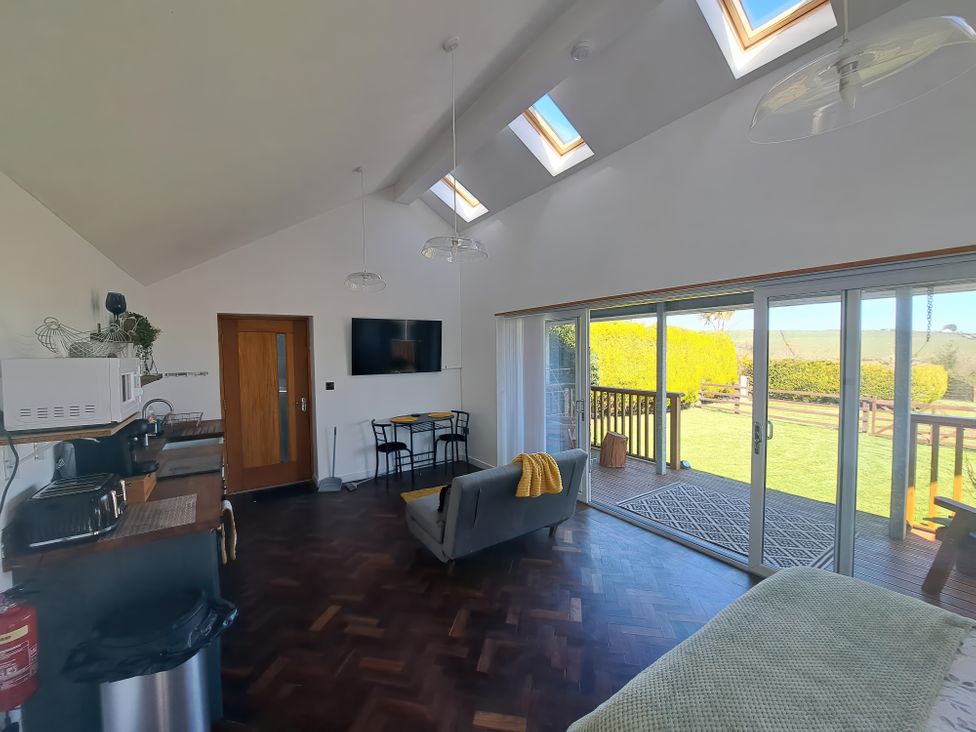 A living room with kitchen area dining table and sliding glass doors opening to a garden at Capel Park (Tyddynod Bach) in Llandyfrydog near Llanerchymedd