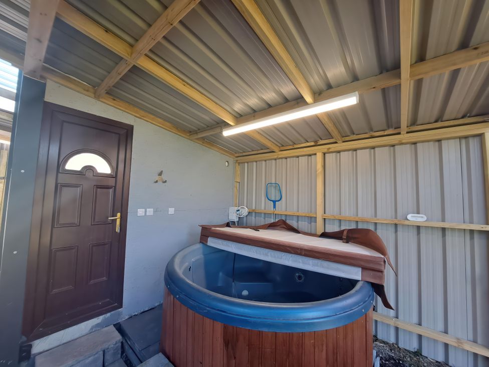 An indoor space with a brown door a round hot tub with a partially removed cover and a net hanging on the wall at Capel Park Tyddynod Bach in Llandyfrydog near Llanerchymedd