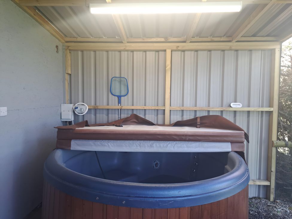 A covered hot tub with a partially removed cover in a shed with a blue pool net hanging on the wall at Capel Park (Tyddynod Bach) in Llandyfrydog near Llanerchymedd