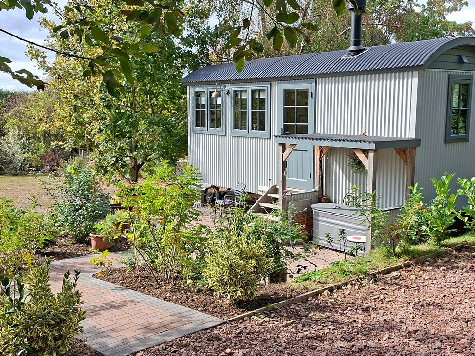 A shed with windows and chimney surrounded by garden at Evendine Hut @ Evendine Cottage, Colwall, Herefordshire