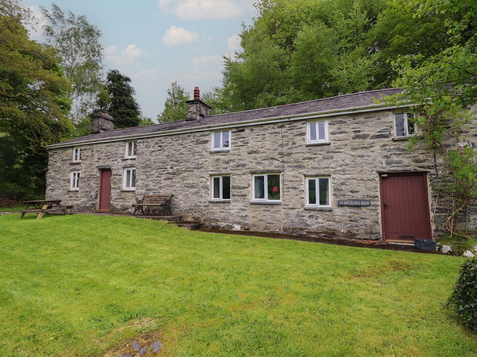 A stone house with a bench and grass area at The Long House in Penmachno