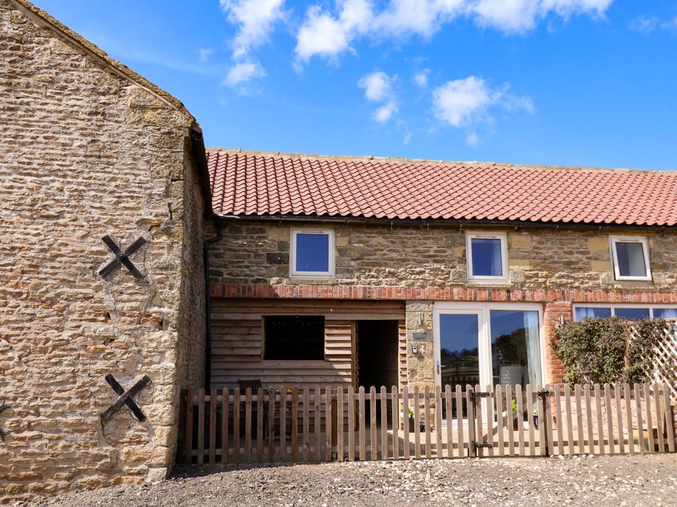 An outdoor view of a stone building with windows and a wooden fence at Hawthorn Cottage in Silpho near Scalby