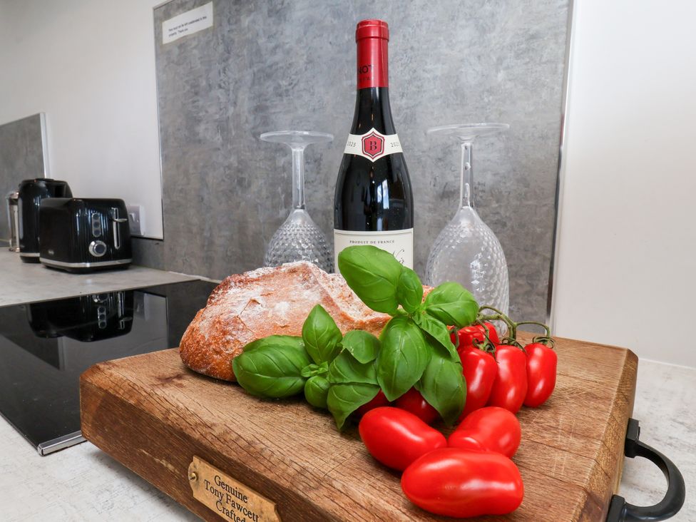 A kitchen with a cutting board, wine bottle, wine glasses, basil, and tomatoes at Hawthorn Cottage in Silpho near Scalby