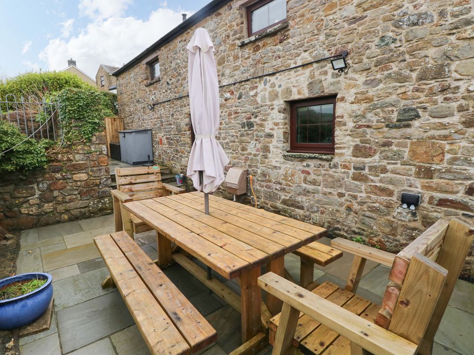 A garden with a wooden table and chairs under an umbrella at The Coach House in Broad Haven