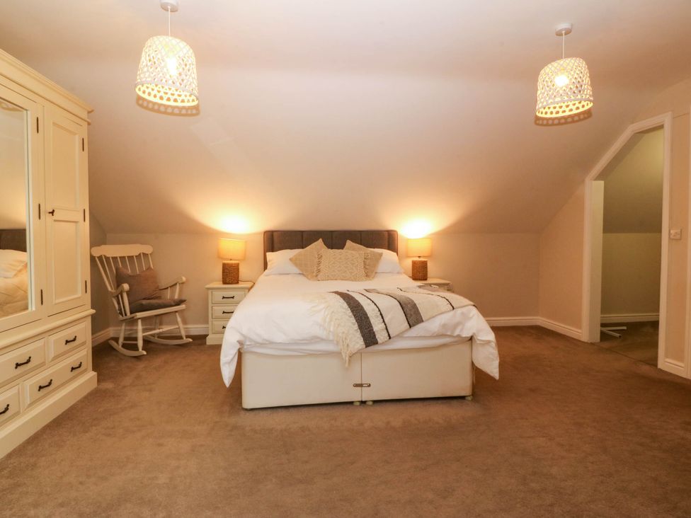 A bedroom with a bed, wardrobe, and rocking chair at Ty Ni Dyffryn Ardudwy