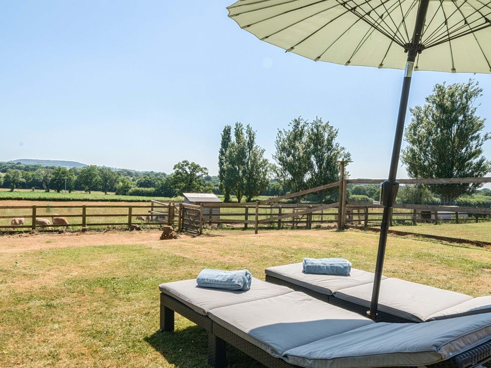 An outdoor area with sun loungers and umbrella at Piglet Corner in Culmstock