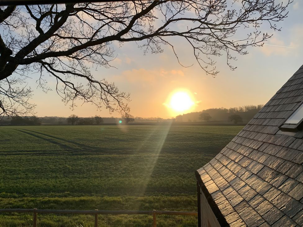 A sunset view over a field with trees and a building roof at 4 Wellacres Cottage Draycott near Moreton-In-Marsh