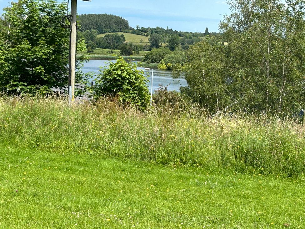 A garden with grass and trees near a body of water at 30 River Run in Belturbet, County Cavan