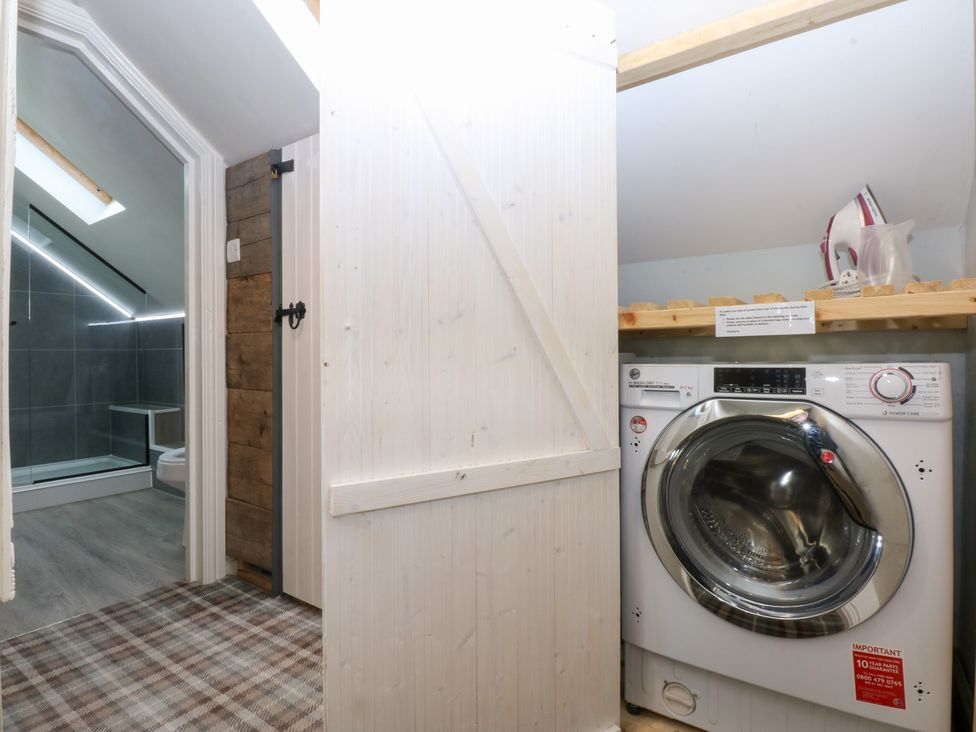 A laundry room with a washing machine and a doorway to a bathroom at Pine Cottage Dinas Dinlle