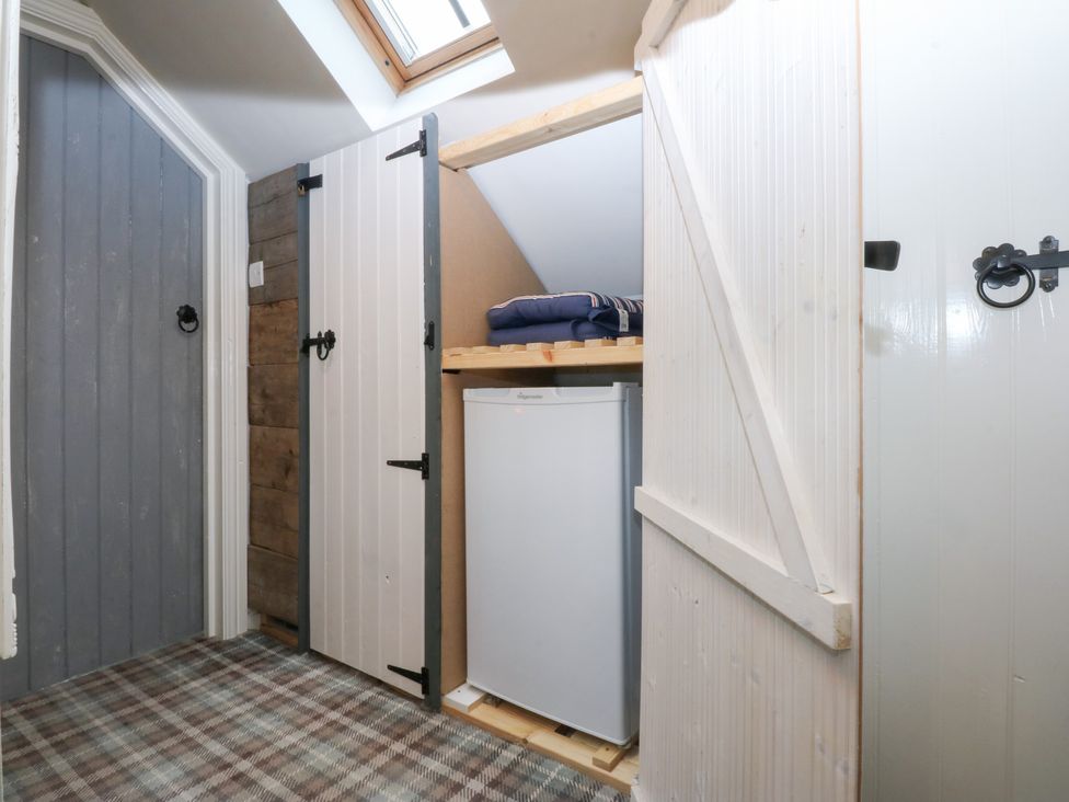 A storage room with a fridge and shelves at Pine Cottage Dinas Dinlle