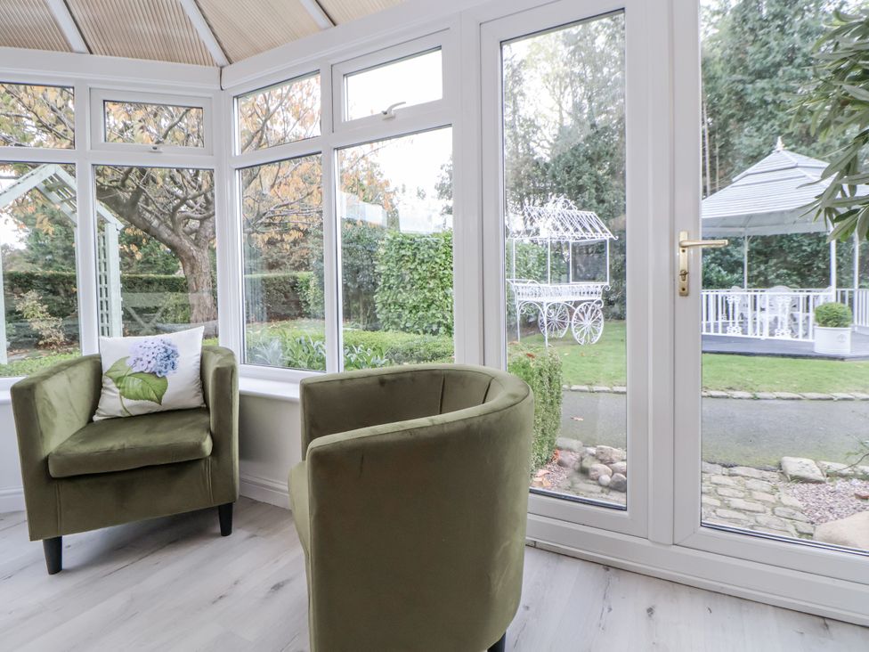 A conservatory with green chairs and garden view at The House at School Farm in Hassall near Haslington