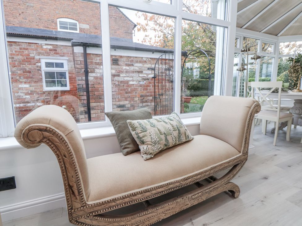 A conservatory with a chaise lounge and cushion at The House at School Farm in Hassall near Haslington