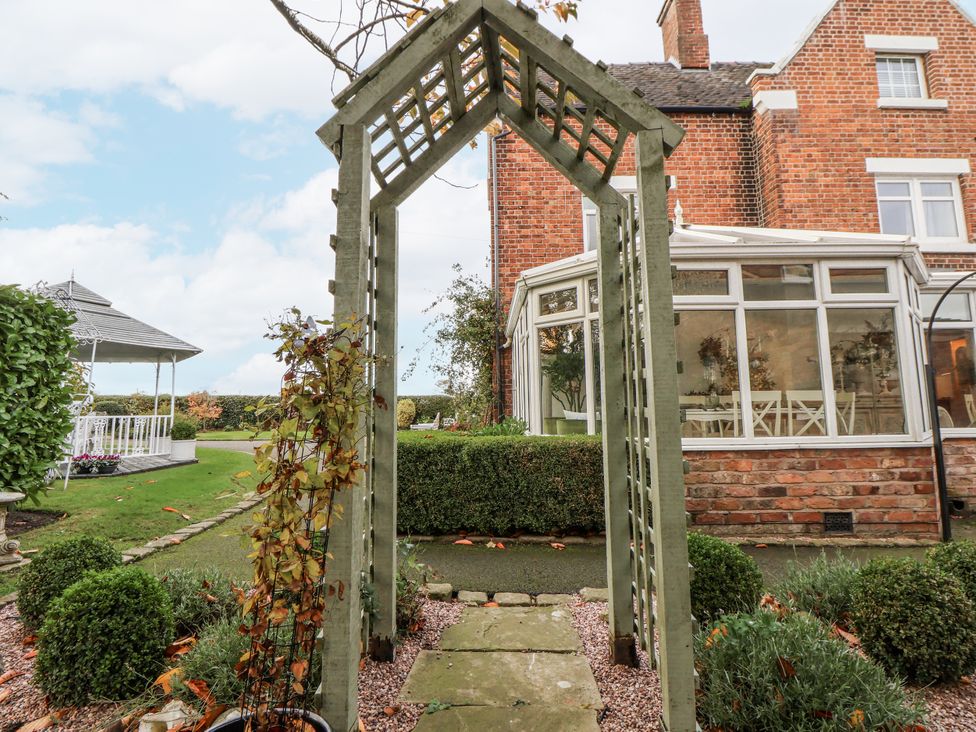 A garden with an archway leading to a conservatory at The House at School Farm in Hassall near Haslington