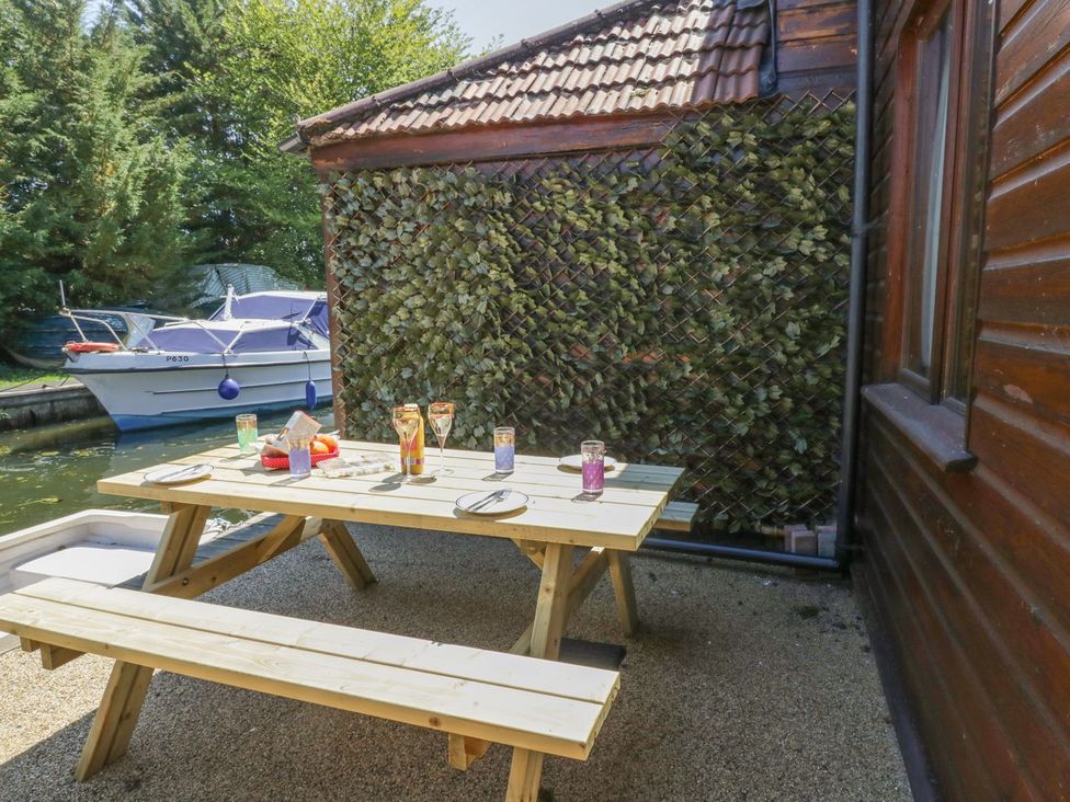 An outdoor seating area with a picnic table and drinks near a boat at Heron Cottage