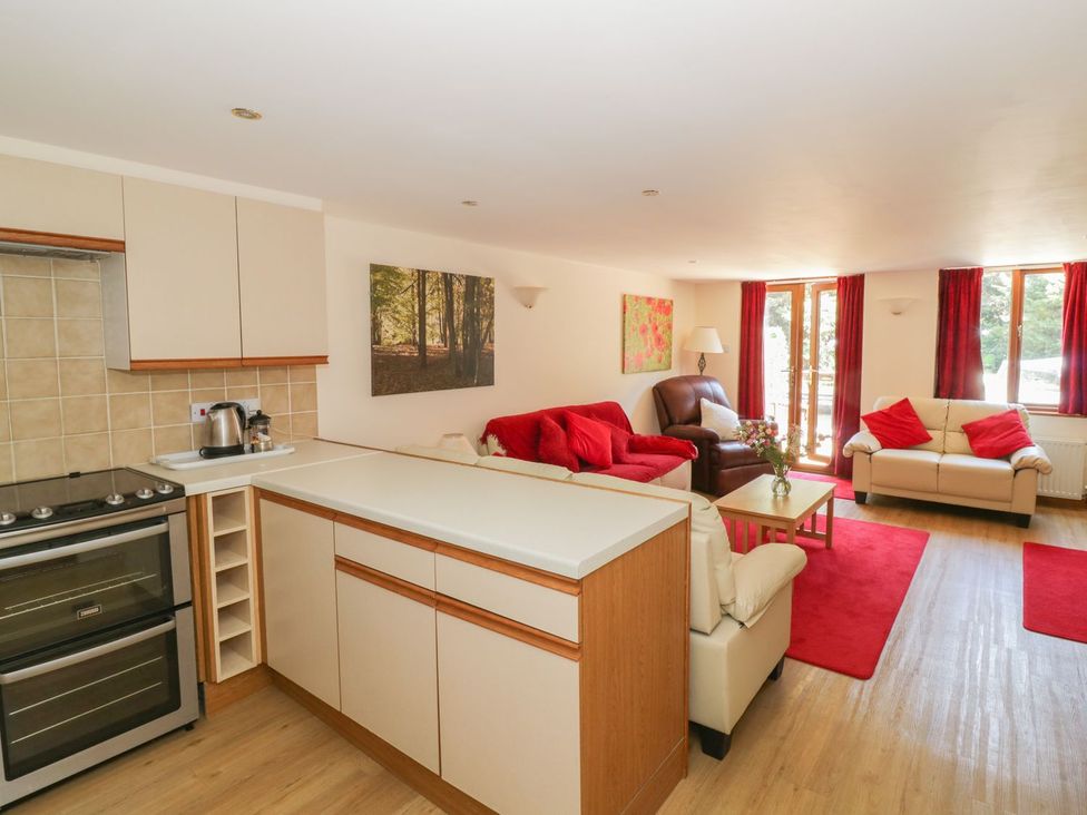 A living room with a kitchen area and seating at Heron Cottage