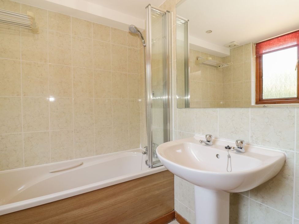 A bathroom featuring a bathtub, shower, sink, and window at Heron Cottage 