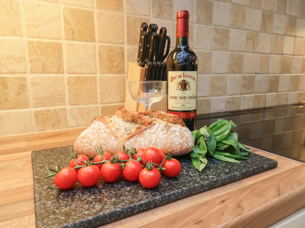 A kitchen with a cutting board containing bread, cherry tomatoes, basil, wine and a glass at Manor Farmhouse in Reighton near Filey