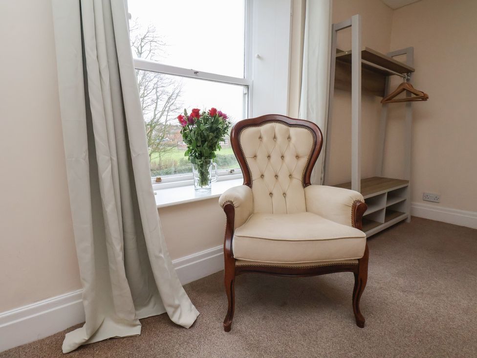 A bedroom with an armchair and flowers on a windowsill at Manor Farmhouse in Reighton near Filey
