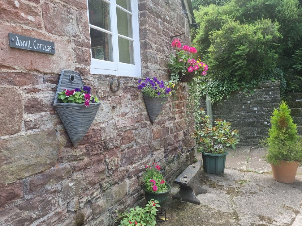 A garden with hanging planters and a stone wall at Anvil Cottage in Gatcombe near Blakeney