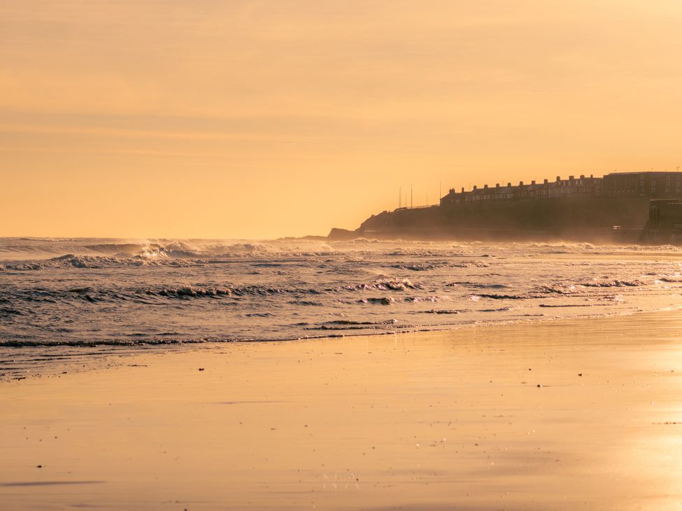 A shoreline with waves and buildings in the background at The George in Whitley Bay