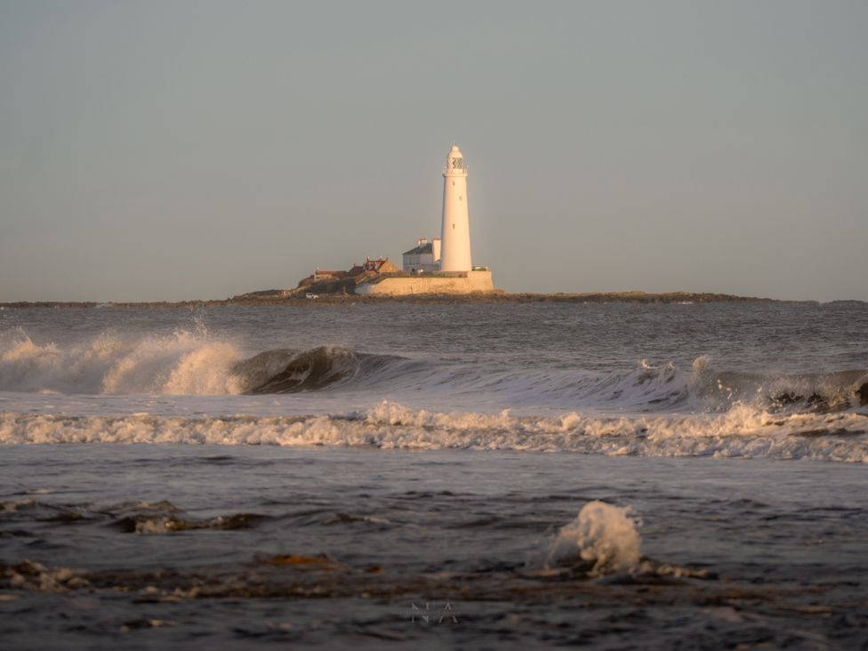 A lighthouse on an island with waves in front at The George in Whitley Bay