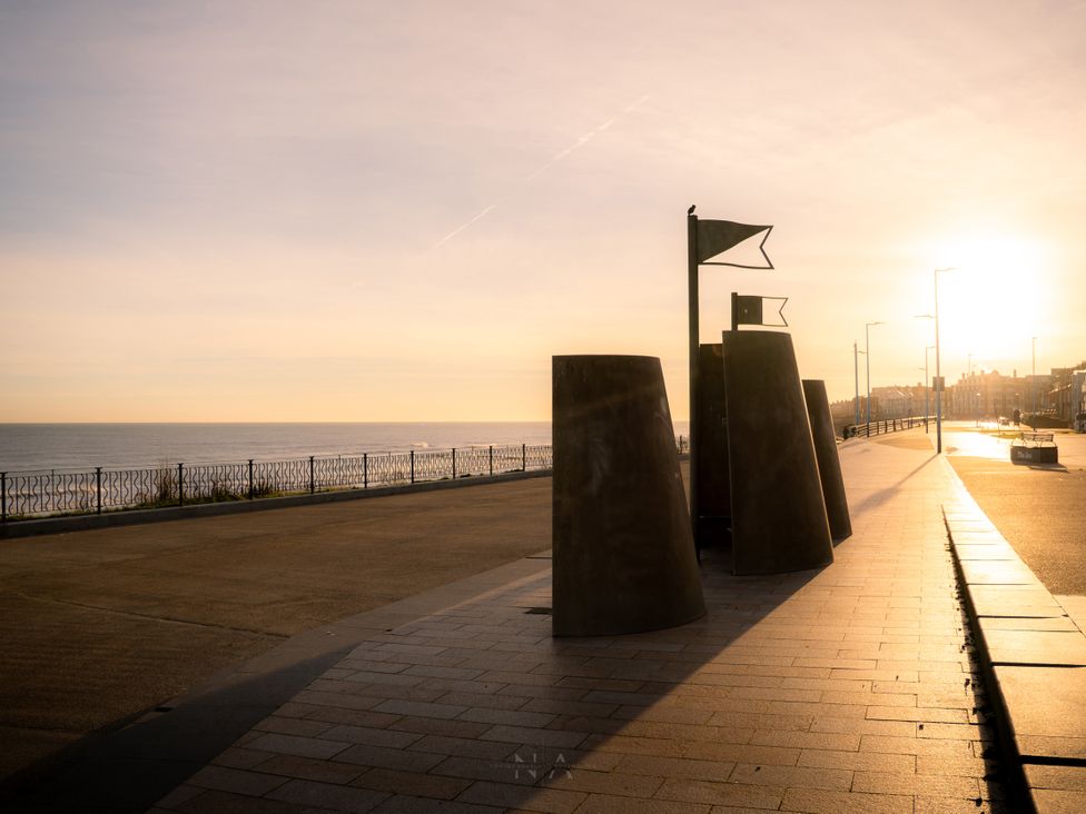 A seafront promenade with seating and a flag pole at The George in Whitley Bay