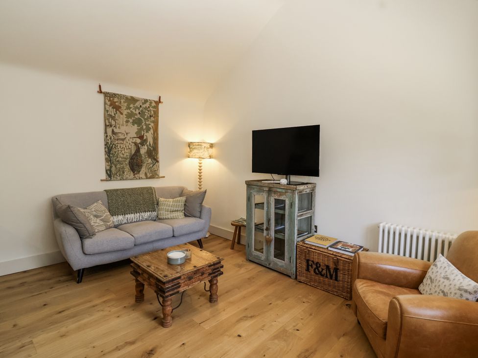 A living room with a sofa, armchair, TV, and coffee table at The Little Loft in Burford