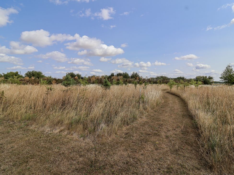 A path through grass and trees under a cloudy sky at The Little Loft in Burford