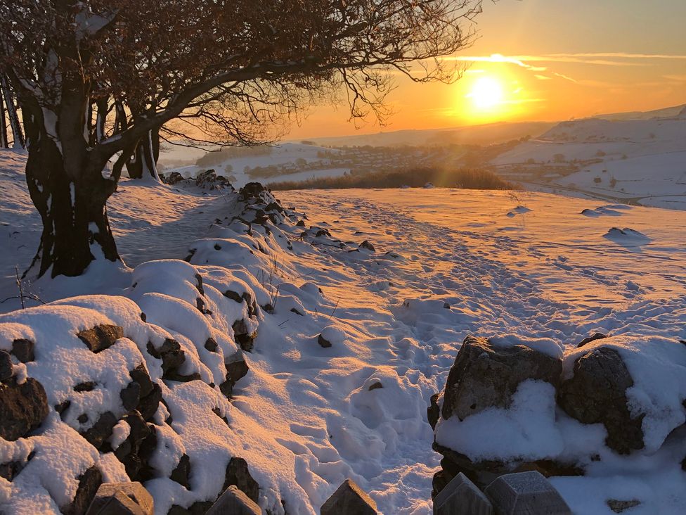 A sunset over snow-covered hills with trees and a rock wall at Woodland View in Buxton